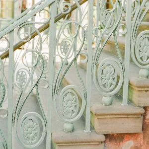 Close-up of ornate wrought-iron staircase, painted in a soft pastel green.