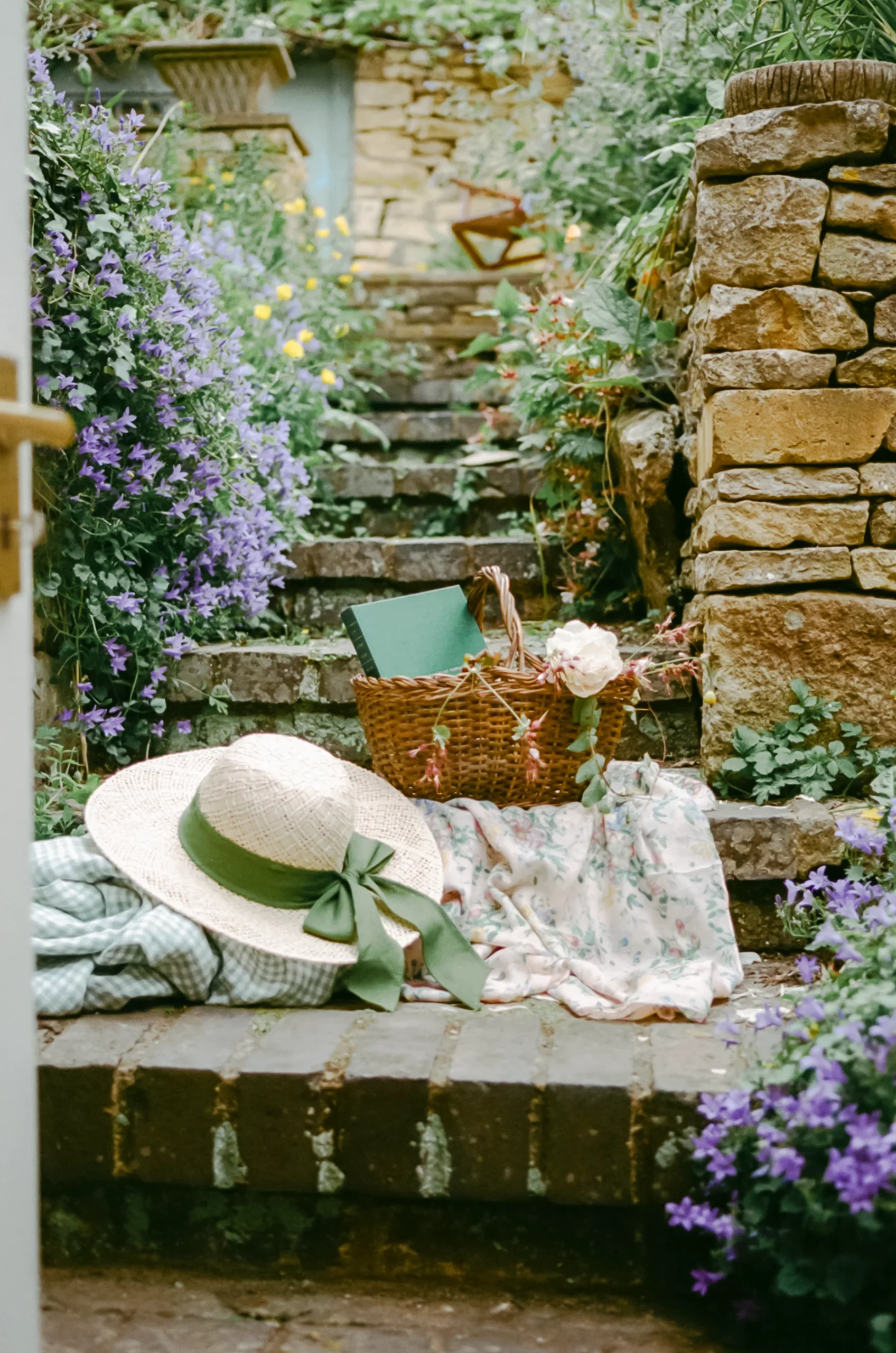 Wicker basket and sunhat on stone steps, with floral fabrics and purple blooms.