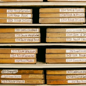 neatly stacked boxes with handwritten labels for various wines, such as Rosé, Bourgogne, and Crémant, in a warm-toned cellar or wine shop.