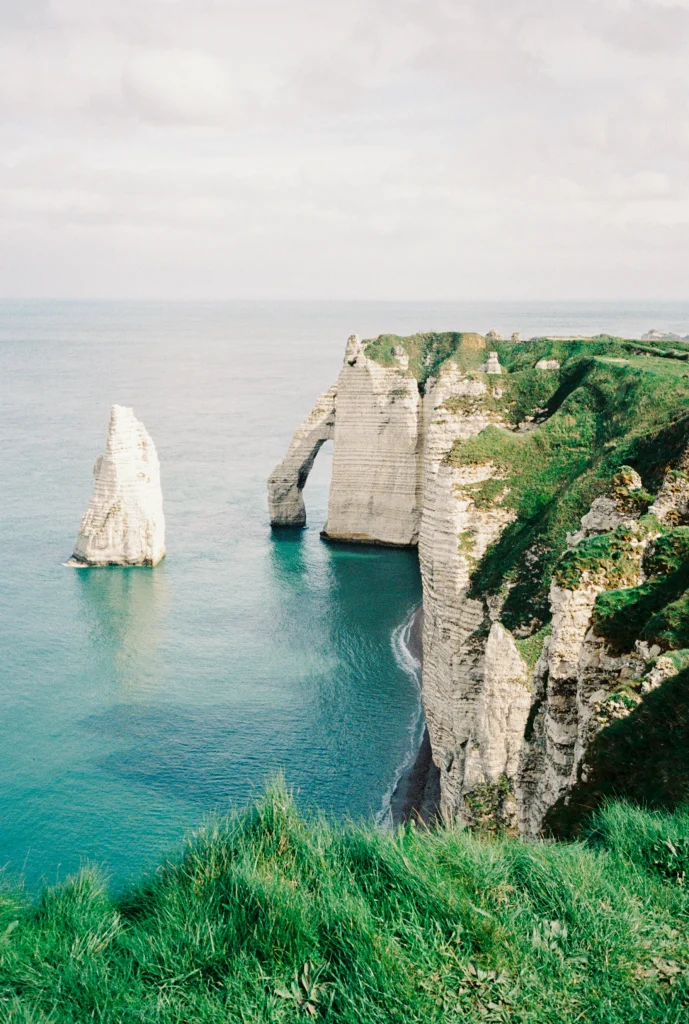 Lone sea stack beside towering cliffs.
