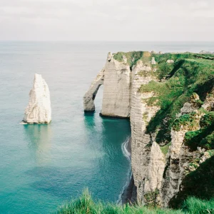 Lone sea stack beside towering cliffs.