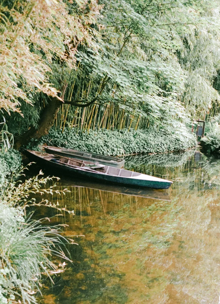 Black boat moored in lush canal – tranquil Europe nature print, peaceful travel wall decor.