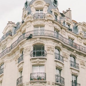Elegant Haussmann-style building with ornate balconies and detailed stonework under a cloudy sky, featuring classic Parisian architecture.